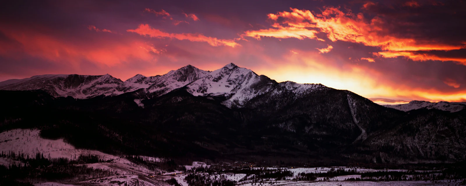 Dusk over the Tenmile Range and a snowy valley in Summit County, Colorado, with a fiery sky